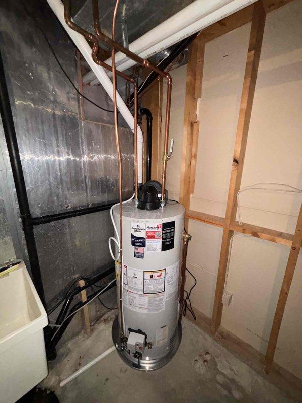 Completed warranty service to replace a plastic water heater drain pan with a metal one as part of previous installation. Relocated gas line closer to ceiling and performed full water heater swap-out in utility area with exposed framing.