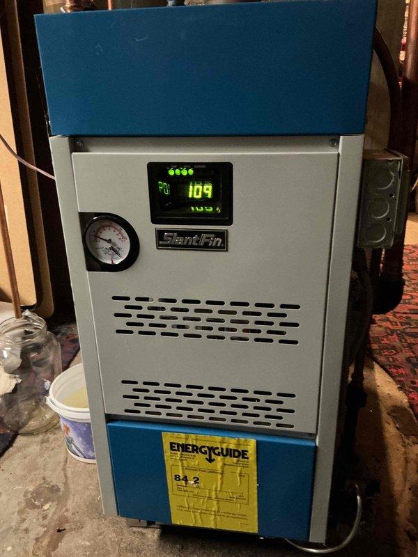 Responded to no heat call for 4-year-old Slant Fin boiler. Diagnosed failed flame rollout switch preventing ignition. Temporarily jumpered switch to test system operation; no actual rollout condition observed during 30-minute test period. Detected minor CO leakage (4ppm) at lower right jacket seal. Replaced rollout switch to restore heat and advised homeowner about potential issues with chimney draft during high winds.