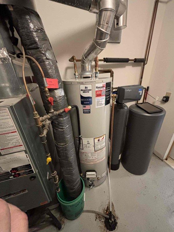 Diagnosed a Richmond 40-gallon natural gas water heater with active tank failure, evidenced by water leaking from the bottom. Informed customer that the unit will need complete replacement due to tank deterioration. Documented installation space containing the failed water heater, adjacent HVAC system, and water treatment equipment for replacement planning.