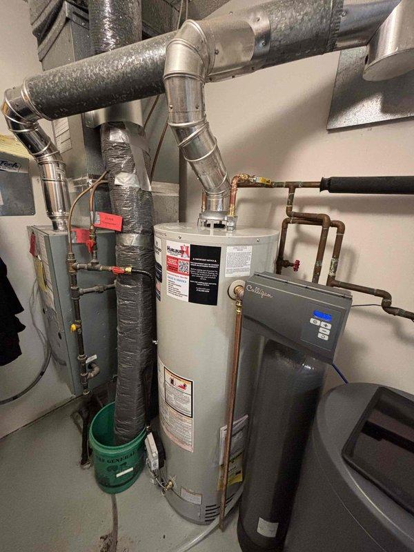 Diagnosed a Richmond 40-gallon natural gas water heater with active tank failure, evidenced by water leaking from the bottom. Informed customer that the unit will need complete replacement due to tank deterioration. Documented installation space containing the failed water heater, adjacent HVAC system, and water treatment equipment for replacement planning.