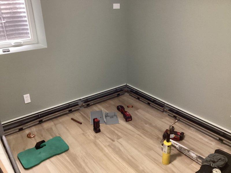 Successfully completed day one of a multi-day hydronic baseboard installation project on the lower level of the home. Began installing various sizes of fin tube baseboard with covers (20', 16', and two 12' sections) in the large room and bedroom. Drained and partially refilled system as part of the ongoing installation process, with work to continue on day two.