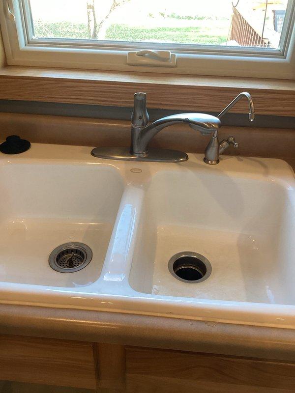 Successfully installed customer-supplied kitchen faucet on white porcelain double-basin sink mounted in wooden countertop. Completed proper connection to existing plumbing system with P-trap drain assembly and verified functionality of main stainless steel faucet with single lever handle and secondary smaller spout for filtered water.
