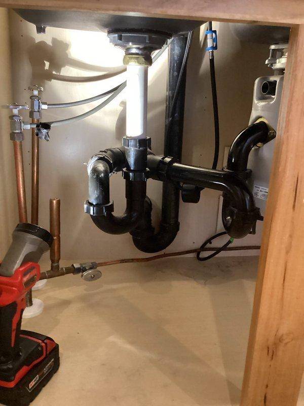 Successfully installed customer-supplied kitchen faucet on white porcelain double-basin sink mounted in wooden countertop. Completed proper connection to existing plumbing system with P-trap drain assembly and verified functionality of main stainless steel faucet with single lever handle and secondary smaller spout for filtered water.