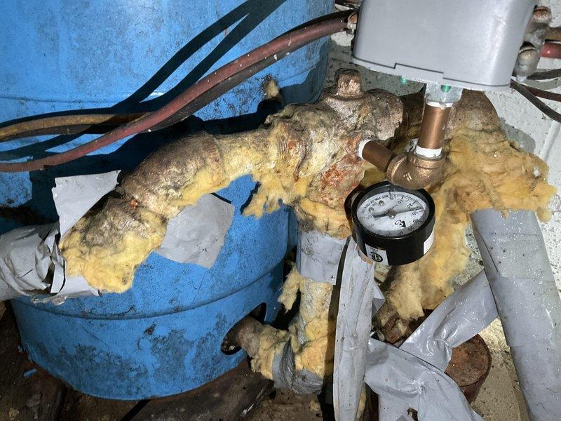 Responded to service call for water leak affecting septic system. Upon inspection, identified significant blue-green corrosion on copper piping at joint connection in utility area. Found deteriorated pipe insulation with visible water damage and worn yellow insulation on connecting lines. Replaced corroded section and installed new fittings to resolve the leak.