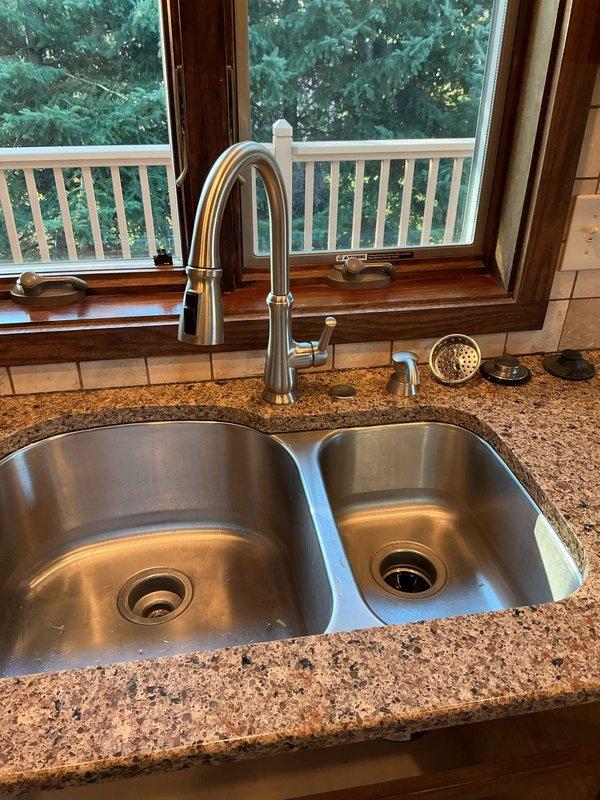 Installed new kitchen faucet and reconnected complete drain assembly including P-trap configuration to double-basin stainless steel sink. Connected copper supply lines to faucet fixture and verified proper drainage system functionality with no leaks present.