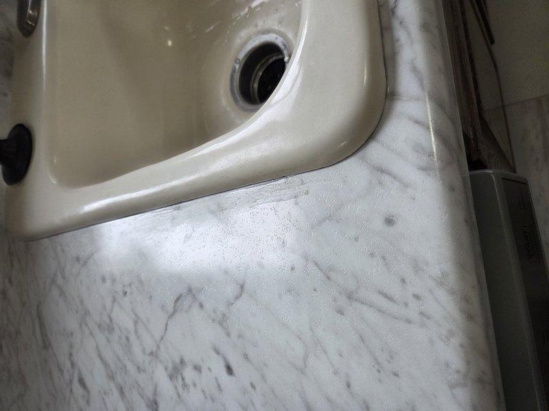 Applied professional-grade silicone caulking around newly installed kitchen sink to create proper water seal. Previous caulking was inadequate; completed high-quality application to ensure watertight junction between sink basin and marble countertop.