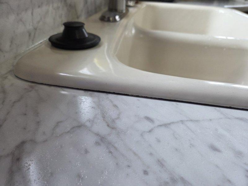 Applied professional-grade silicone caulking around newly installed kitchen sink to create proper water seal. Previous caulking was inadequate; completed high-quality application to ensure watertight junction between sink basin and marble countertop.