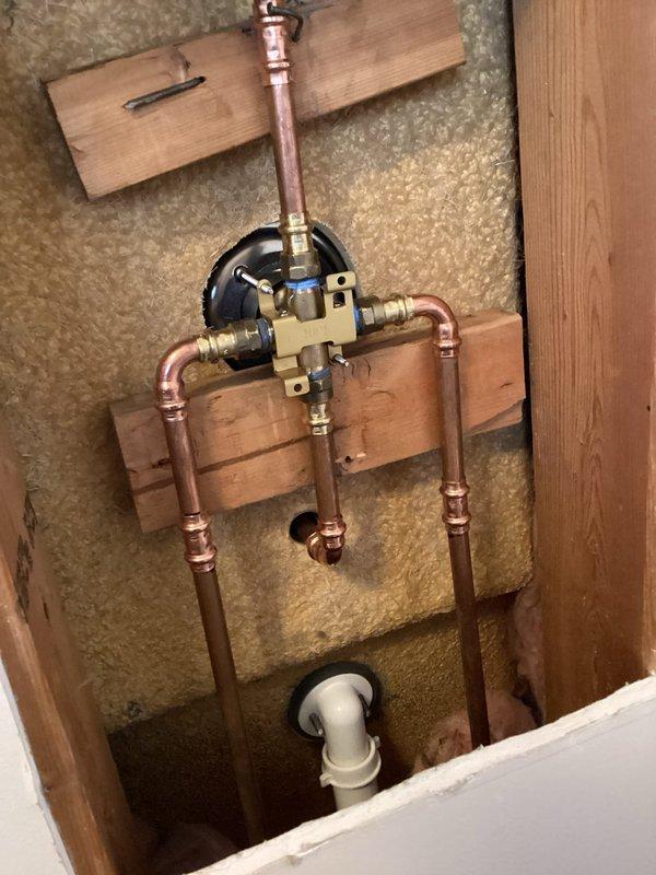 Successfully installed customer-supplied tub shower valve, spout, and shower head through existing wall access. Work included mounting brass mixing valve assembly on wooden support with proper copper pipe connections. No warranty provided on customer-supplied parts as per company policy.
