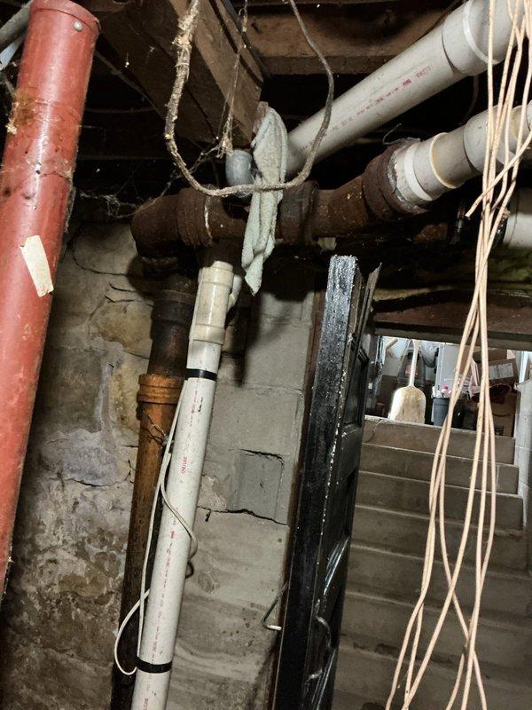 Responded to service call for smart toilet overflowing and leaking from base. Upon inspection, discovered main 4-inch drain line was completely blocked at transition to cast iron pipe. Observed significant deterioration at pipe connection point. Cut open pipe to drain standing water, then made temporary repair to restore functionality. Submitted bid for permanent repair solution due to observed corrosion and deterioration of cast iron waste pipe junction.