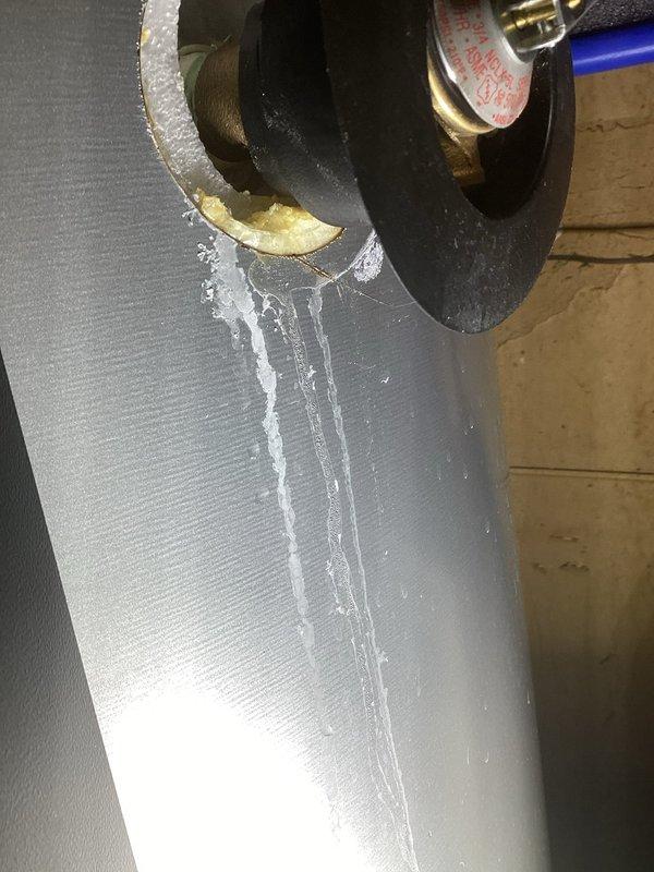 Responded to service call for 1-year-old electric water heater leaking from bottom. Inspection revealed water actively streaming from brass valve connection on supply line with mineral buildup indicating ongoing leak. Determined tank failure requires complete replacement. Informed homeowner of warranty options through original retailer (Home Depot) as unit was not installed by our company.