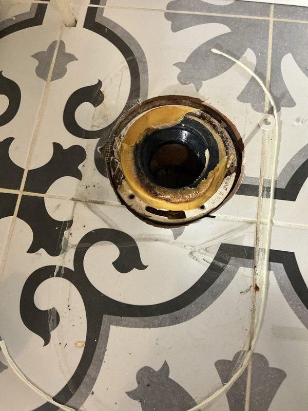 Removed toilet to investigate leak affecting downstairs bathroom. Inspection revealed deteriorated toilet flange with significant mineral buildup and corrosion. Flange showed signs of water damage with discoloration around edges, suggesting ongoing leak issue. Found wax ring compromised and requiring replacement.
