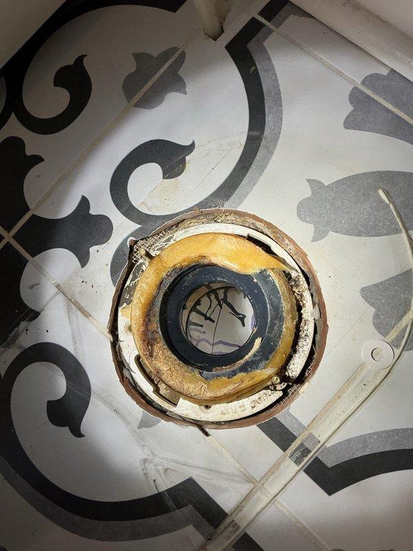 Removed toilet to investigate leak affecting downstairs bathroom. Inspection revealed deteriorated toilet flange with significant mineral buildup and corrosion. Flange showed signs of water damage with discoloration around edges, suggesting ongoing leak issue. Found wax ring compromised and requiring replacement.