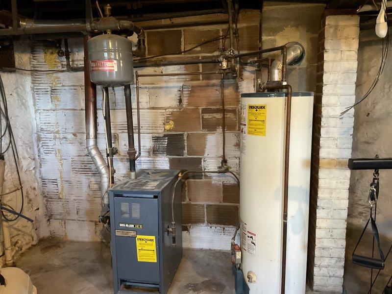 Inspected 27-year-old 40-gallon gas water heater with standard vent that was experiencing no hot water pressure. Observed significant water damage and mold on surrounding walls indicating long-term moisture issues. Assessed aging system components including expansion tank and connecting copper piping network. Equipment was functional but at end of service life, requiring replacement to restore proper hot water pressure.