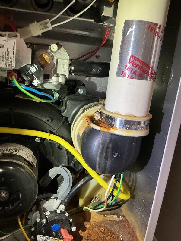 Repaired HVAC system by applying silicone sealant to compromised rubber coupling between inducer motor and vent pipe. Identified significant corrosion at the connection point where black elbow joint meets the white PVC vent pipe. Temporary repair completed; scheduled return visit to replace the deteriorated 90-degree rubber boot assembly.