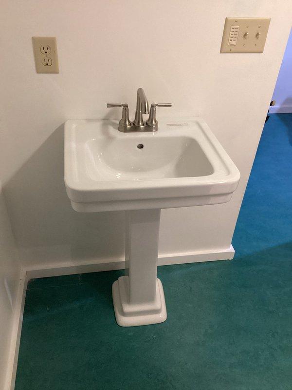 Completed installation of customer-supplied pedestal sink and toilet in bathroom, which included properly connecting water supply lines, drain pipes, and ensuring secure fixture mounting. Installation required accessing ceiling plumbing in utility area to properly route PVC drainage and copper water supply lines for the new bathroom fixtures.