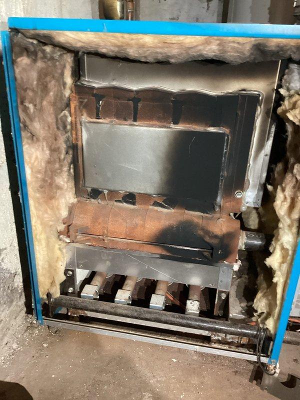 Responded to emergency no-heat call where customer reported smoking and flames inside their aging boiler. Investigation revealed combustion issues caused by insulation material that had been pulled into the burner orifice area by a rodent, preventing proper burning. Removed insulation debris, performed standard boiler service, and cleaned flame sensor to restore proper operation. System functioning normally upon departure but recommended replacement of pilot assembly if intermittent pilot issues persist.