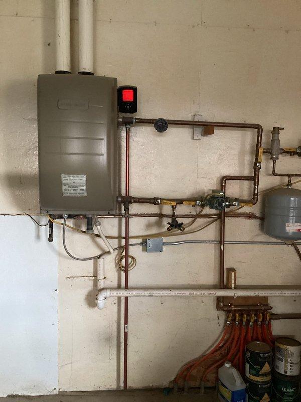 Responded to a service call for a non-functioning boiler serving in-floor heat in shop area. Diagnostic testing confirmed igniter functionality and proper gas pressure, but combustion failure persisted. Inspection revealed a dead bird obstructing the exhaust vent, preventing proper ventilation. Disassembled exhaust components, removed blockage, and reassembled system. Upon restart, boiler ignited and operated normally. System includes wall-mounted tankless unit with copper distribution piping and PEX manifold configuration for radiant floor heating.