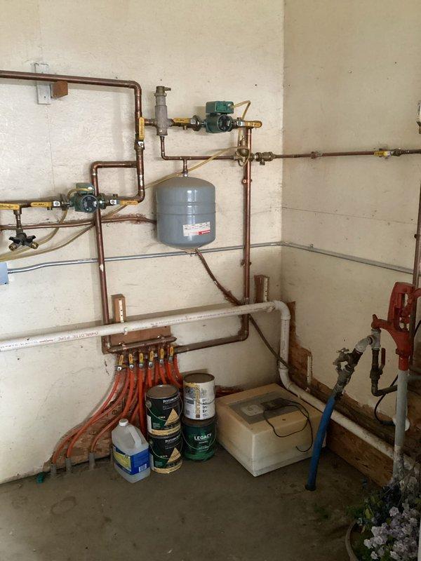 Responded to a service call for a non-functioning boiler serving in-floor heat in shop area. Diagnostic testing confirmed igniter functionality and proper gas pressure, but combustion failure persisted. Inspection revealed a dead bird obstructing the exhaust vent, preventing proper ventilation. Disassembled exhaust components, removed blockage, and reassembled system. Upon restart, boiler ignited and operated normally. System includes wall-mounted tankless unit with copper distribution piping and PEX manifold configuration for radiant floor heating.