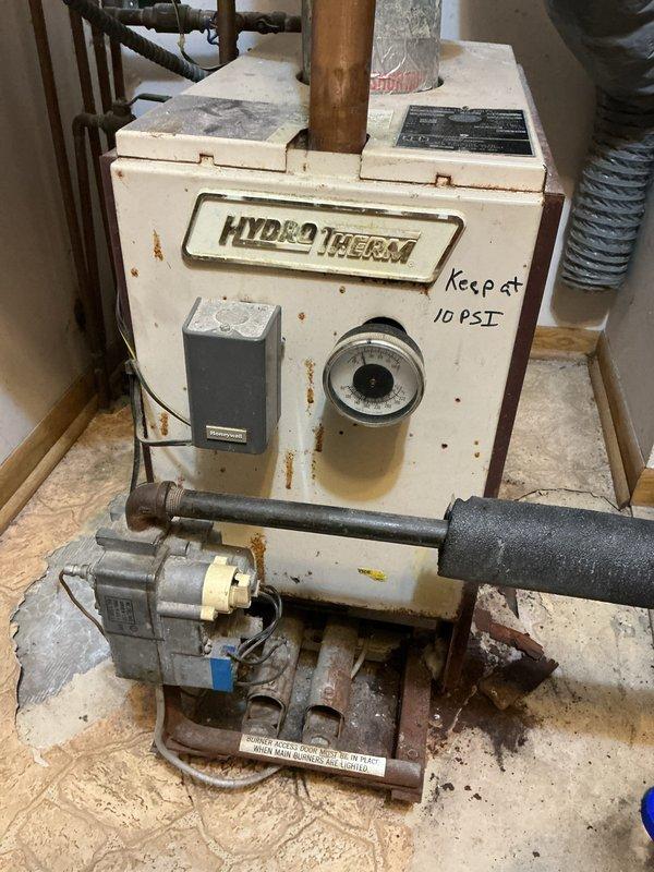 Inspected 30+ year old Hydro Therm natural gas boiler system that was functioning but experiencing water distribution issues. Verified boiler operation was normal despite customer's complaint about inconsistent heating in back bedroom. Customer has mini-splits installed as backup heating and prefers to maintain current system rather than replace aging unit. Noted handwritten instruction to "Keep at 10 PSI" on pressure gauge.