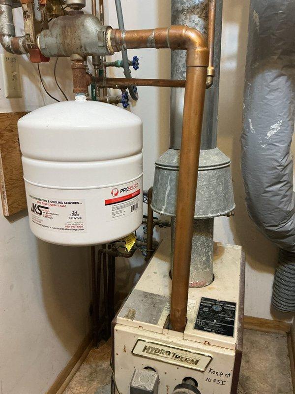 Inspected 30+ year old Hydro Therm natural gas boiler system that was functioning but experiencing water distribution issues. Verified boiler operation was normal despite customer's complaint about inconsistent heating in back bedroom. Customer has mini-splits installed as backup heating and prefers to maintain current system rather than replace aging unit. Noted handwritten instruction to "Keep at 10 PSI" on pressure gauge.