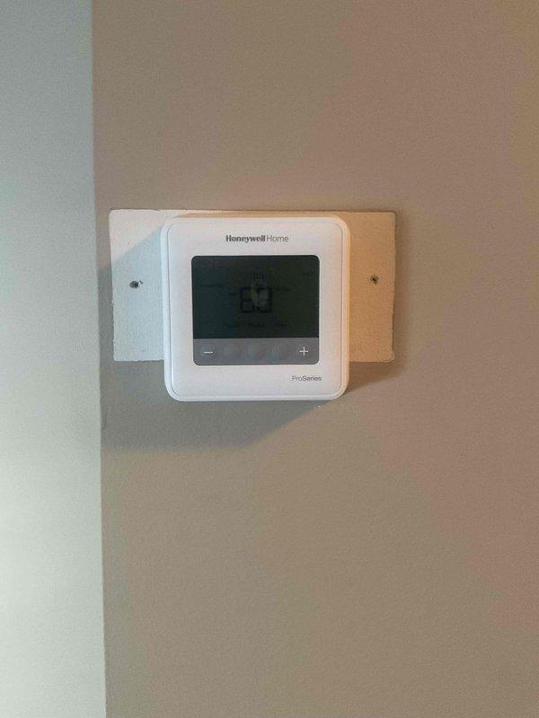 Responded to client request to remove the white backplate from Honeywell Home ProSeries thermostat for aesthetic purposes. Successfully removed backplate as requested, leaving thermostat properly mounted and functioning at 63°F. Client will have painter husband complete any cosmetic touchups to the wall.