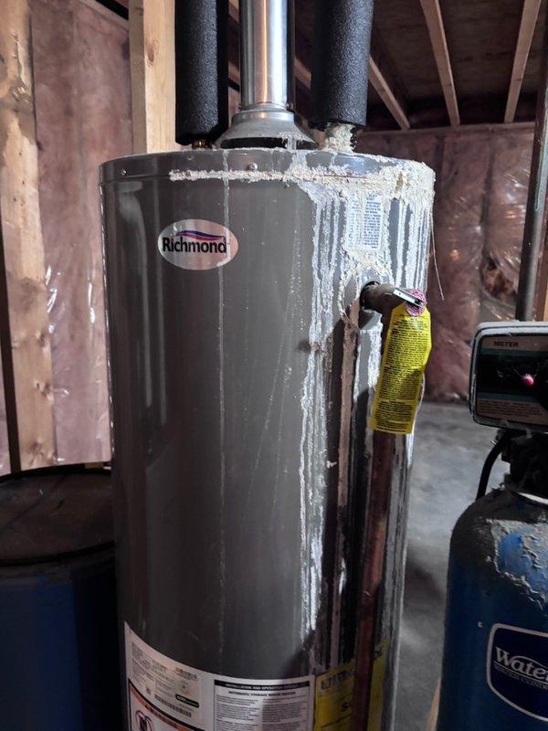 Successfully installed customer-supplied LP gas water heater (Richmond model) in unfinished basement area. Properly connected black insulated pipes to the top of the unit and positioned the heater adjacent to customer's blue WaterMate tank. Noted presence of mineral deposits on exterior of tank, likely from previous unit.