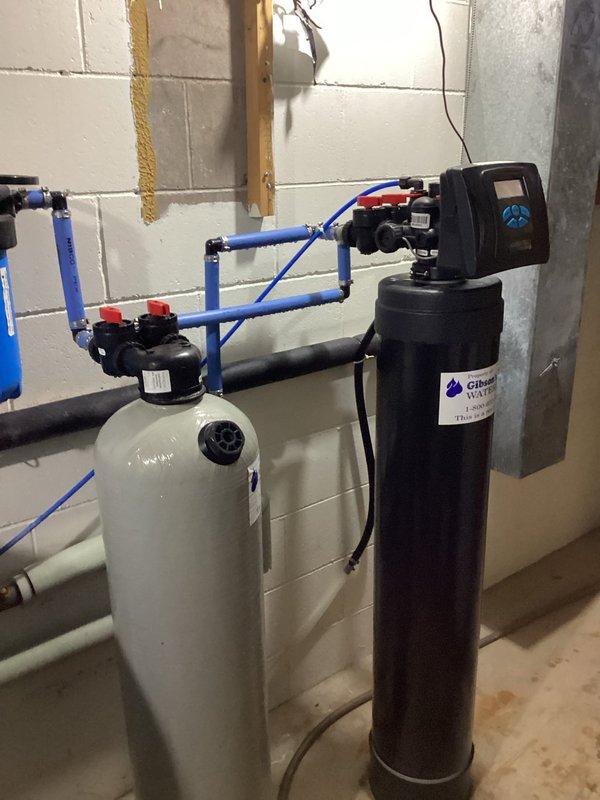 Responded to an emergency service call for a leaking air eliminator on a tanked water heater. Upon inspection, determined that specialized heating expertise was required rather than standard plumbing service. Documented the water treatment system installation and affected copper piping assembly showing significant oxidation and mineral deposits. Referred case to heating technician per supervisor's direction.