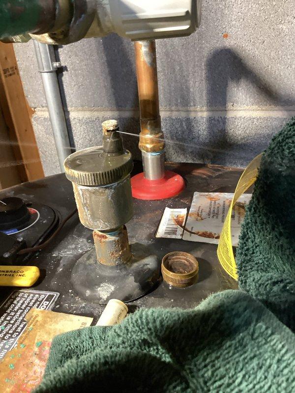 Responded to an emergency service call for a leaking air eliminator on a tanked water heater. Upon inspection, determined that specialized heating expertise was required rather than standard plumbing service. Documented the water treatment system installation and affected copper piping assembly showing significant oxidation and mineral deposits. Referred case to heating technician per supervisor's direction.