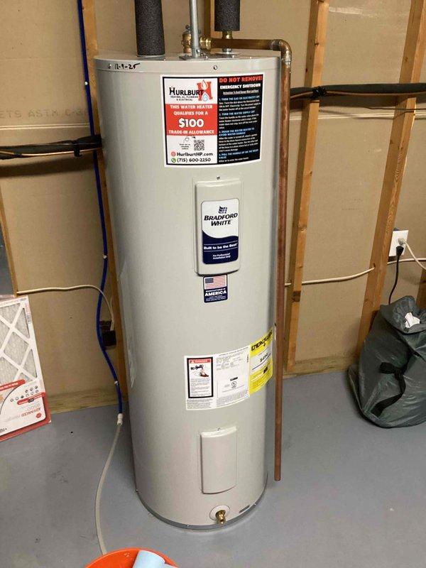 Replaced leaking 50-gallon Bradford White water heater showing significant rust and corrosion streaks from access panel to drain valve. New unit installed in utility area with proper copper and insulated pipe connections to existing plumbing system.