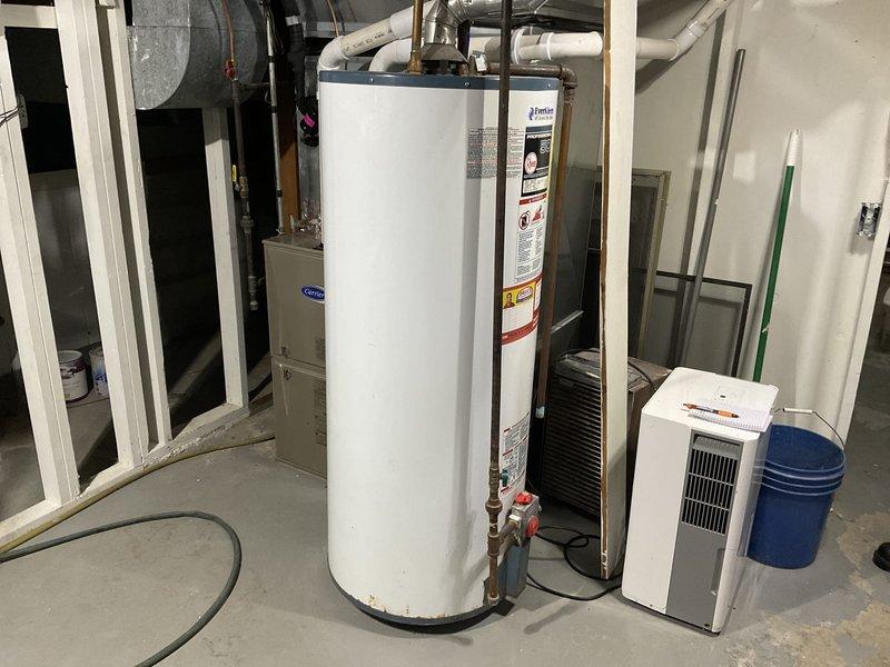 Conducted inspection of existing 50-gallon standard water heater system and surrounding installation environment to provide estimates for replacement options. Assessed current setup in utility room which included the water heater alongside Carrier furnace and dehumidifier unit. Also evaluated ceiling/wall access points for potential tankless or power vent installation, documenting all findings with detailed photographs.