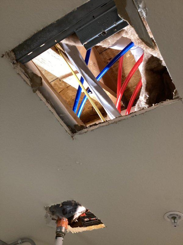 Responded to commercial water leak complaint originating from unit 210's tub valve where maintenance work was being performed with an incompletely closed shut-off valve. Discovered white water pipe with hole in ceiling above walk-in cooler causing water intrusion. Accessed ceiling space through inspection openings to assess plumbing infrastructure and electrical components potentially affected by water damage.