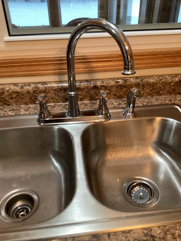 Installed homeowner-supplied kitchen faucet with side sprayer in double-basin stainless steel sink. Assessed basement toilet installation but determined customer's Tuscany model was incompatible with existing high flange; substituted with Gerber toilet for proper fit and function. Boxed customer's original toilet and placed in their vehicle.