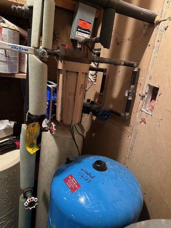 Replaced main house water valve and installed new water filtration housing in residential utility area. System includes blue pressure tank and beige sediment filter, with all connections properly secured and tested for functionality.