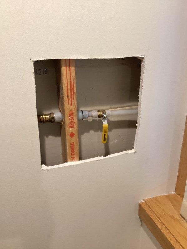 Accessed leaking hose bibb through interior wall cutout, revealing connection to primary plumbing system with pressure-treated support structure. Replaced faulty hose bibb and installed new white access panel for future maintenance, resolving leak that was penetrating wall.