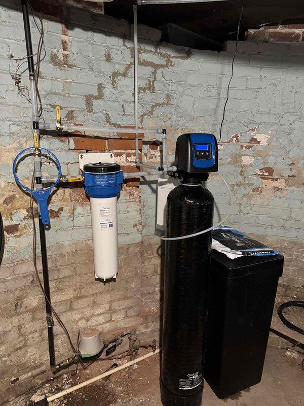 Installed new water treatment system in basement, including a water softener with brine tank and a carbon filter with spindown functionality. Water hardness measured at 14 ppm. System includes a Water Care treatment package and required cutting a trap into the existing drain in the crawl space for proper drainage connectivity.