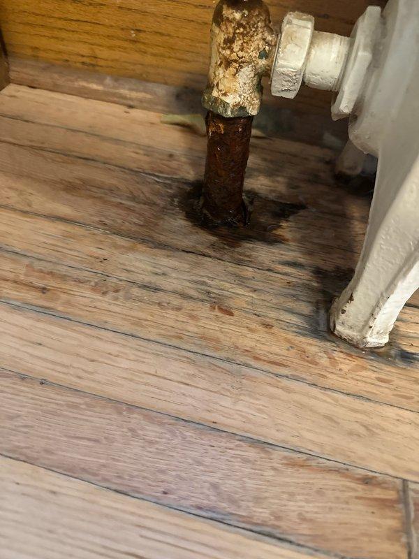 Responded to service call for radiator system issues. Inspected and found a severely corroded pipe elbow at radiator connection with active leak and significant water damage to surrounding wooden flooring. Replaced deteriorated radiator valve and repiped connection point, followed by bleeding all four radiators in the system to restore proper operation.