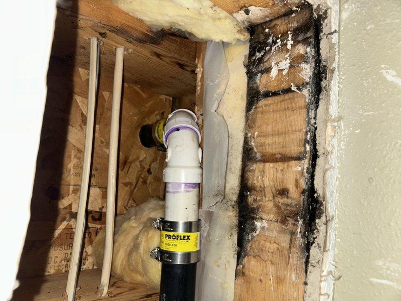 Responded to call regarding kitchen sink drain leaking into basement ceiling. Upon inspection, located source of leak in kitchen drain line. Removed section of wall to access the affected area, replaced damaged pipe section with new PVC fittings and secured with PROFLEX clamp. Observed water damage and possible mold on surrounding wooden framing.