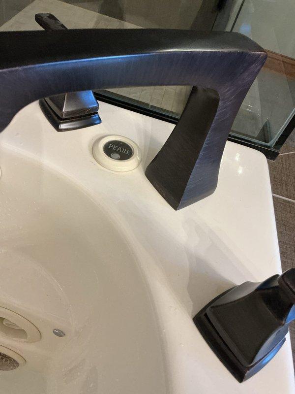 Conducted annual plumbing inspection of bathroom fixtures. Examined multiple sinks including a white porcelain basin with dark metallic faucet and a beige composite sink with oil-rubbed bronze three-piece fixture set. All fixtures were functioning properly with no leaks or damage observed.