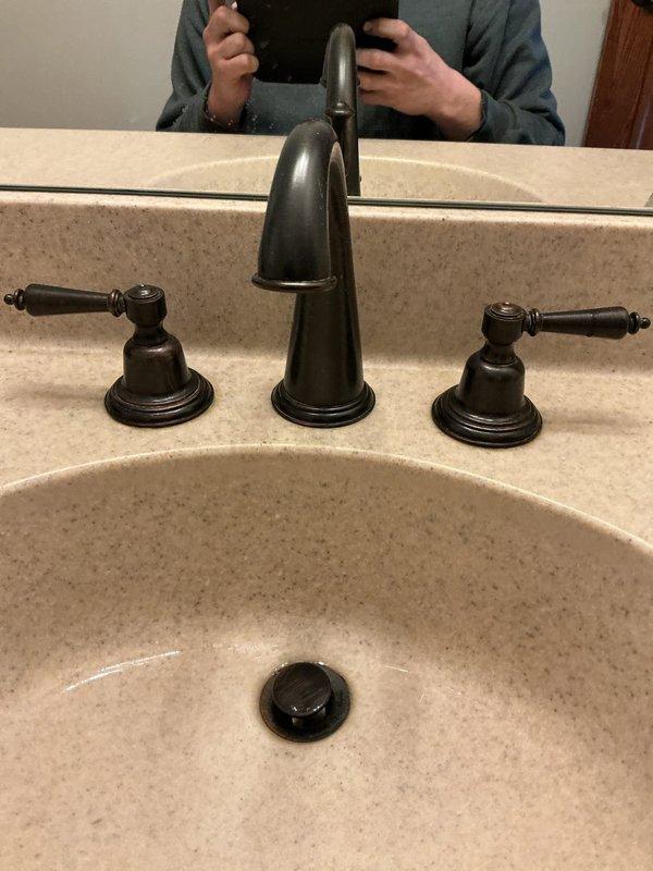 Conducted annual plumbing inspection of bathroom fixtures. Examined multiple sinks including a white porcelain basin with dark metallic faucet and a beige composite sink with oil-rubbed bronze three-piece fixture set. All fixtures were functioning properly with no leaks or damage observed.