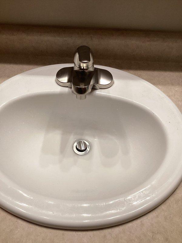 Successfully installed customer-supplied lavatory faucet in bathroom sink. Removed old two-handle chrome fixture showing signs of tarnishing and water spots, and properly installed new fixture with clean connections. Verified proper operation with no leaks after installation.