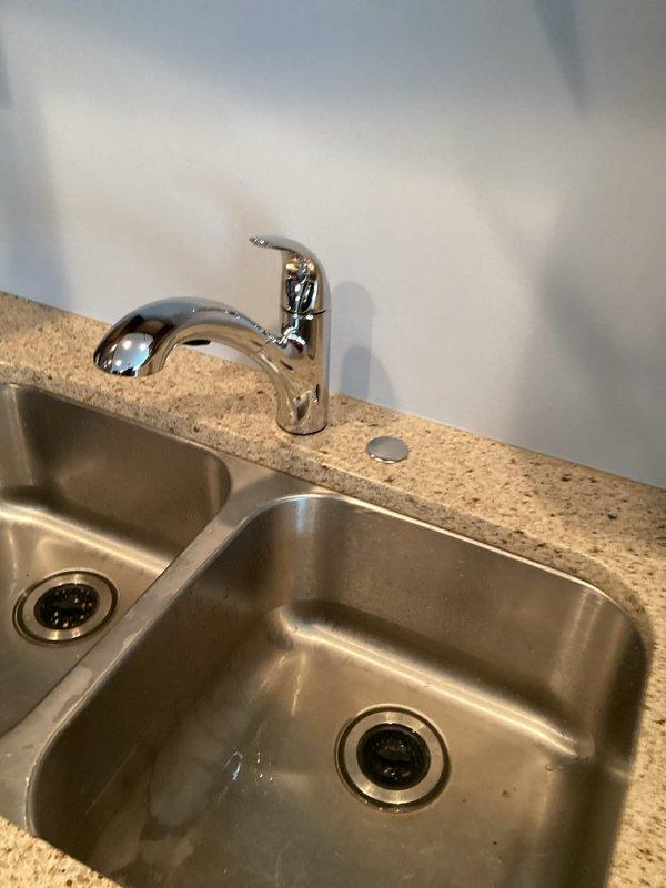 Successfully installed customer-supplied kitchen faucet in a double stainless steel sink mounted in beige granite/composite countertop. Completed installation of main chrome fixture with high arched neck and single lever handle, ensuring proper function and no leaks.