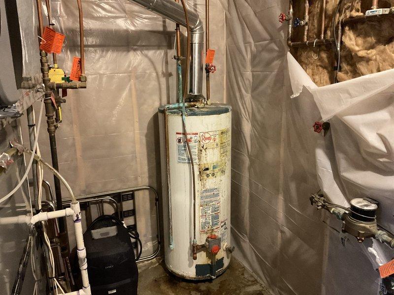 Performed assessment of 33-year-old 40-gallon gas water heater showing significant deterioration including tank bottom rusting, extensive corrosion/lime buildup, and an improperly installed saddle valve on the hot water line to humidifier causing severe leakage. Recommended replacement with 50-gallon natural gas standard vent water heater based on home size (2300 sq ft) and occupancy (3-4 residents).