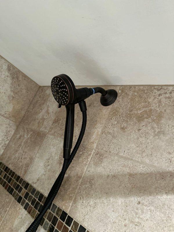 Successfully installed dual-head shower fixture with dark bronze finish in tiled shower enclosure. Unit includes a primary fixed shower head with multiple spray nozzles and secondary handheld shower head with flexible hose. Installation completed as sold with all components functioning properly.
