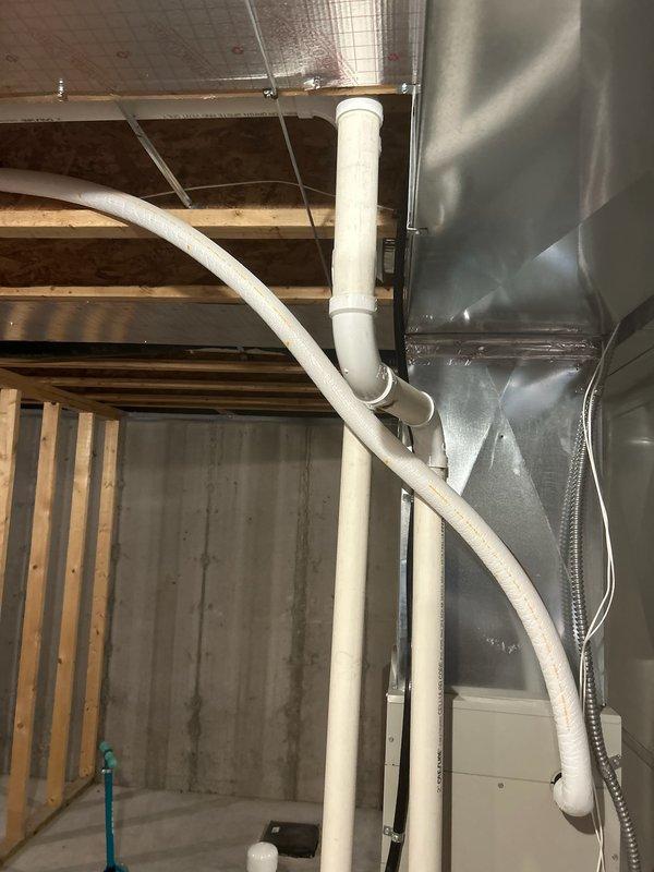 Assessed basement construction project where lineset from furnace to exterior conflicts with planned bathroom framing. Documented current installation with exposed PVC plumbing, metal ductwork, and copper lineset routing issues. Relocation of copper line required; recommended scheduling installation team to determine appropriate rerouting solution for HVAC components.