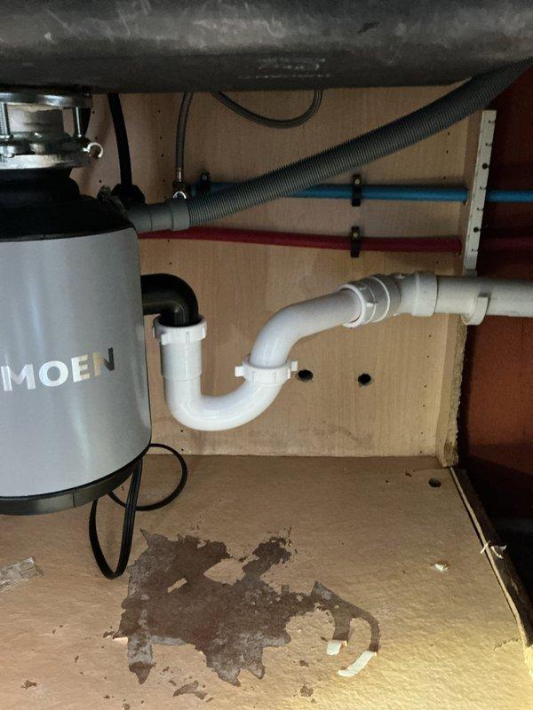 Repaired kitchen sink drain leak by installing new P-trap assembly. Previous improper drain line connection had caused water damage to cabinet base, evidenced by visible staining. Ensured proper connection to existing Moen garbage disposal unit and verified leak-free operation of the new installation.