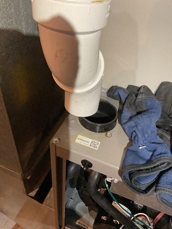 Performed annual maintenance on 1-year-old furnace, which revealed improper installation of exhaust components. Discovered PVC pipe was not properly secured with glue/silicone to draft inducer, causing exhaust leakage at connection point and 45° elbow. Removed compromised section, installed new fittings with proper adhesive application, and applied silicone around street fitting in draft flue. System tested for 25 minutes with no further leaks detected.