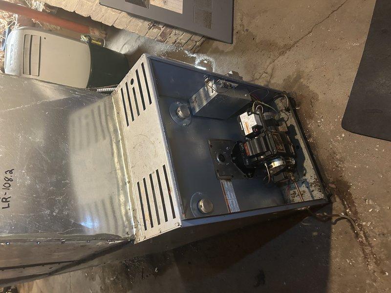 Responded to no-heat complaint on oil furnace that was in lockout condition. Upon inspection, found nozzle heavily clogged and approximately 1" of standing water in work area. Performed maintenance including nozzle replacement and filter replacement, noting non-standard filter assembly configuration. After initial service, unit continued to exhibit same symptoms. Tested CAD cell with no improvement. Diagnosed need for primary control replacement; parts ordered for follow-up service.