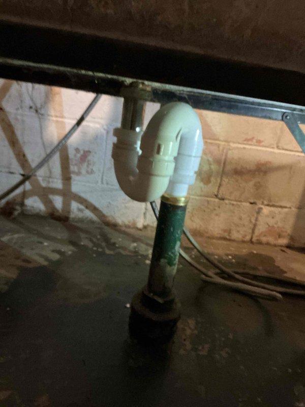 Responded to service call for laundry tub leak in basement. Inspection revealed failing S-trap assembly with visible corrosion on the brass drain pipe. Removed deteriorated components and replaced with new PVC P-trap configuration, properly connecting to existing drainage system. Verified proper operation with no leaks after installation.