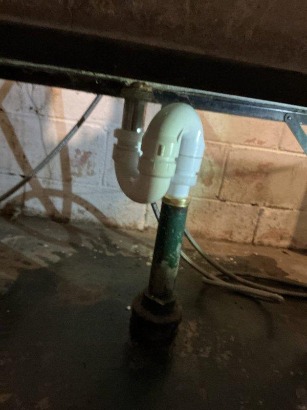 Responded to service call for laundry tub leak in basement. Inspection revealed failing S-trap assembly with visible corrosion on the brass drain pipe. Removed deteriorated components and replaced with new PVC P-trap configuration, properly connecting to existing drainage system. Verified proper operation with no leaks after installation.