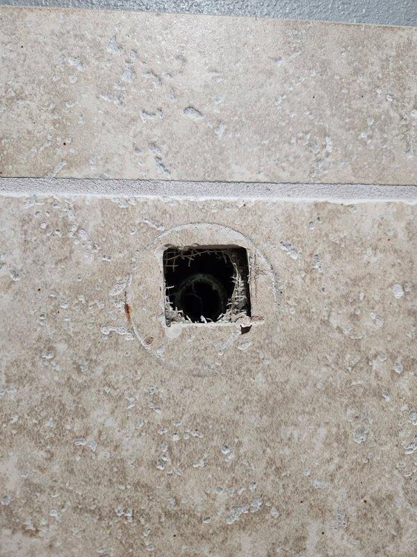 Accessed shower plumbing through cut access hole in tile to address pipe failure. Found corroded copper fitting with broken shower head and threads stuck inside eared ell. Replaced damaged 90-degree elbow fitting to restore proper shower functionality.